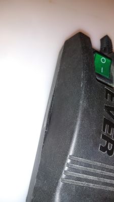 Zbliżenie na czarną obudowę listwy z zielonym włącznikiem i widoczną szczeliną między częściami.
