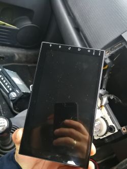 Osoba trzyma czarne radio LED z Androidem w samochodzie Mitsubishi Colt.