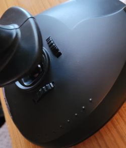 Podstawa czarnego joysticka z widocznym uchwytem i dwoma pokrętłami na obudowie, ustawiona na drewnianym blacie.