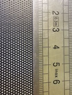 Close-up of perforated metal mesh next to a metric ruler with millimeter scale