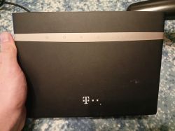 Czarny router Huawei z logo T‑Mobile, trzymany w dłoni na tle dywanu