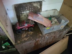 A flooded room with damaged equipment, including a red toy car and a container full of electronic parts.