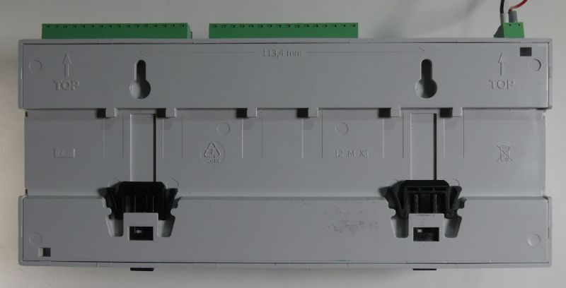 Tył szarego modułu elektrycznego z zielonymi listwami zaciskowymi i czarnymi zatrzaskami