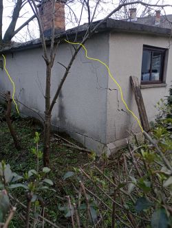 Zdjęcie przedstawia zewnętrzną ścianę garażu z widocznymi pęknięciami oznaczonymi żółtymi liniami.
