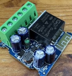 Intelligenter Schalter mit Relais und Kondensatoren Nahaufnahme eines intelligenten Schalters mit schwarzem Relais und blauen Kondensatoren auf einem Holzuntergrund.