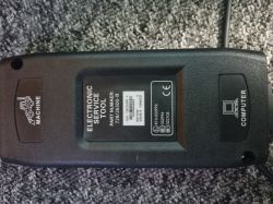 Elektroniczne narzędzie serwisowe leżące na dywanie z dwoma portami oznaczonymi jako MACHINE i COMPUTER.