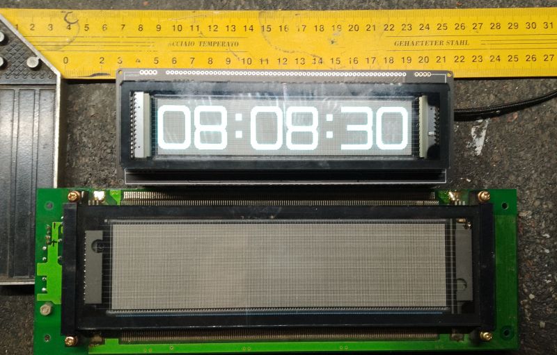 Wyświetlacz VFD z dużymi cyframi zegara pokazujący czas 08:08:30, leżący na tle miarki.