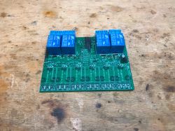 Printed circuit board with four relays mounted on a workbench.