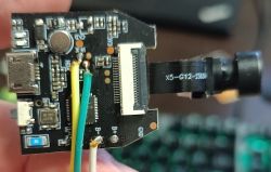 Close-up of a PCB with a micro USB port, two wires, and a small cylindrical camera module