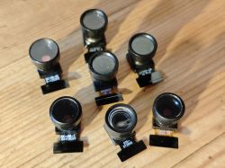 Seven small camera modules lying on a wooden surface