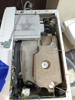 Wnętrze pralki z widocznymi elementami mechanicznymi i elektrycznymi.
