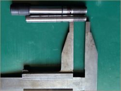 Dwa metalowe wałki leżące obok suwmiarki na zielonym tle.