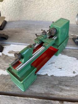 Miniaturowy model zielonej maszyny tokarskiej na drewnianym tle.