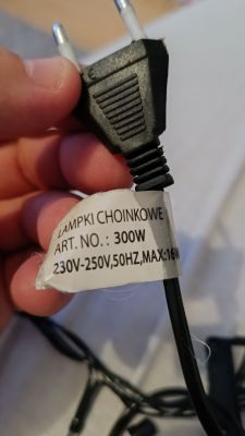 Zbliżenie na wtyczkę elektryczną lampek choinkowych z etykietą przedstawiającą parametry techniczne.