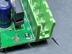 Uszkodzony bezpiecznik SMD na zielonej płytce PCB obok złącza śrubowego