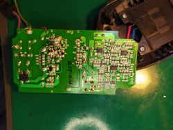 Płytka drukowana ładowarki Parkside PLCP-016A z widocznymi elementami elektronicznymi oraz ścieżkami, leżąca na zielonej macie serwisowej.