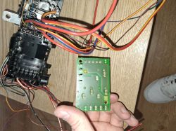 Person holding a green printed circuit board with wires and an electronic component on a wooden table.