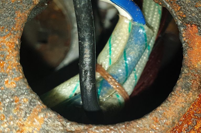 Zbliżenie na kable wewnątrz metalowego elementu z rdzawymi śladami.