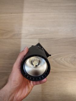 Osoba trzyma reflektor LED na tle podłogi z jasnego drewna.