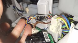 Wnętrze urządzenia z wiązką przewodów i małą płytką elektroniki wpiętą w złącza