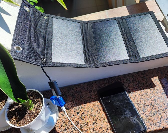 Rozłożony panel słoneczny ładuje telefon przez miernik USB na słonecznym balkonie