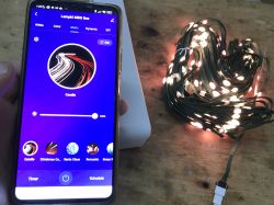 LED Christmas Lights Control App Smartphone with LED light control app next to Christmas lights on a wooden table.