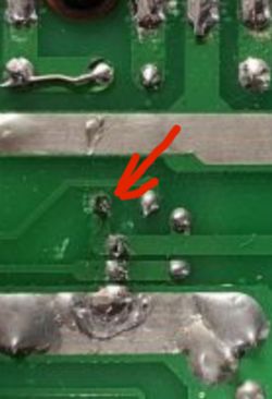 Zbliżenie na płytkę PCB z widocznymi punktami lutowniczymi, wskazanymi czerwoną strzałką.