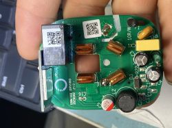 PCB held in a hand, with a relay, copper-wound coils, capacitors, and QR-code stickers