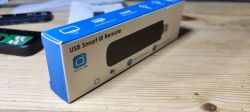USB Smart IR Remote Packaging Box of USB Smart IR Remote lying on a wooden table.