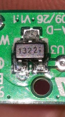 Zbliżenie elementu SMD z napisem „1327” na zielonej płytce PCB obok otworu montażowego