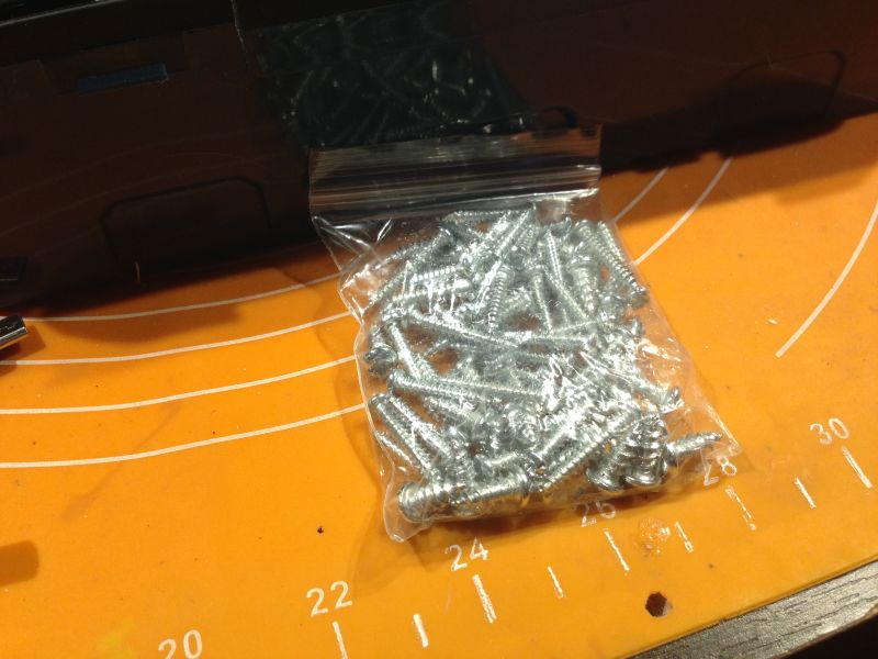 Zbliżenie na woreczek foliowy z metalowymi wkrętami na pomarańczowej macie.