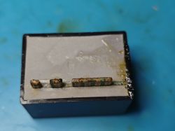 Burned power module with white potting compound, showing damaged output pins