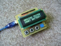 Wyświetlacz LCD na płytce Arduino z napisem ARDUINO TESTER SMART BATTERY!, podłączony przewodem USB, z trzema przyciskami i niebieskim czujnikiem.