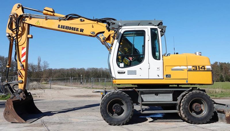 Żółta koparka kołowa Liebherr 314 na placu, widok z boku.