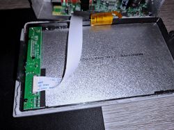 Wnętrze urządzenia z metalową osłoną i zieloną płytką PCB po lewej, połączone taśmą