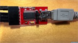Red FTDI adapter with a USB cable inserted, on a wooden table background.
