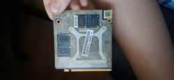 Moduł komputerowy GPU lub CPU trzymany w dłoni, z widoczną etykietą i pamięciami