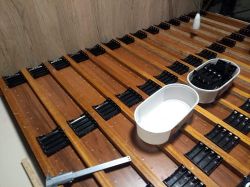 Wooden energy storage frame with rows of black plastic battery holders, two white containers with additional connectors on the surface.