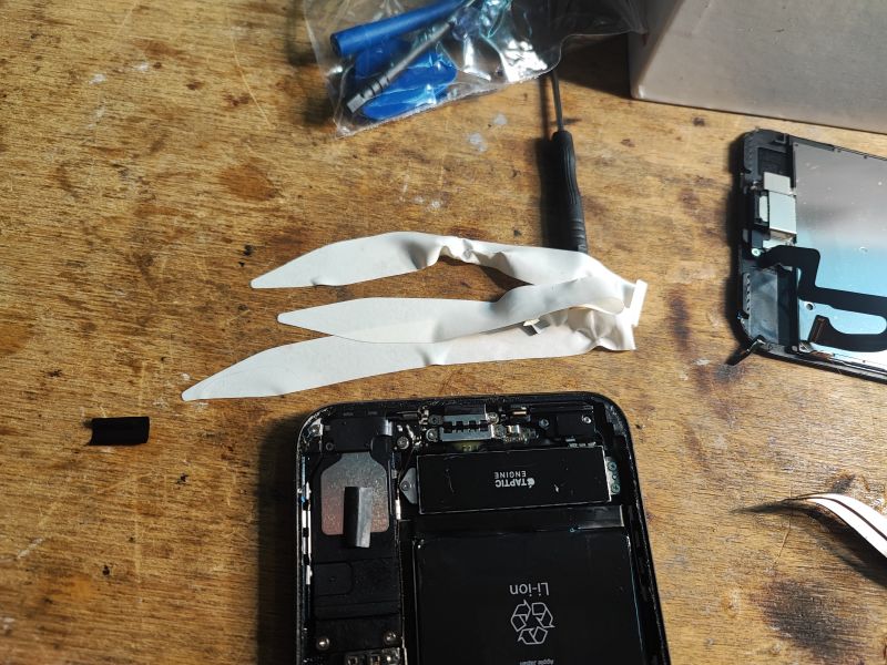 iPhone Battery Replacement - Disassembly Steps Disassembled iPhone on a wooden table with visible adhesive strips.