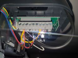 Zbliżenie na wnętrze urządzenia elektronicznego z kablami podłączonymi do kostki zaciskowej.