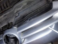 Zbliżenie na przedni grill samochodu z widoczną plastikową kratką i brakującym znaczkiem.