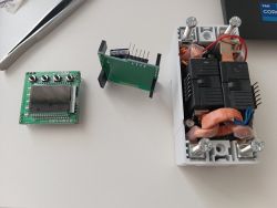 Electronics on a desk: PCB with LCD and buttons, a pin-header board, and an open power module with copper windings