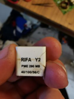 Kondensator RIFA Y2 z pęknięciem na obudowie trzymany w dłoni.