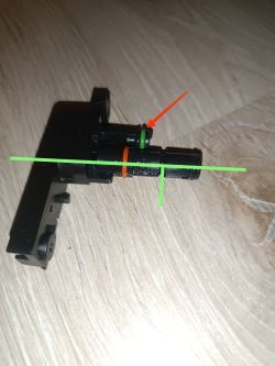 Zbliżenie na plastikowy element z oznaczeniami zielonymi i czerwoną strzałką.