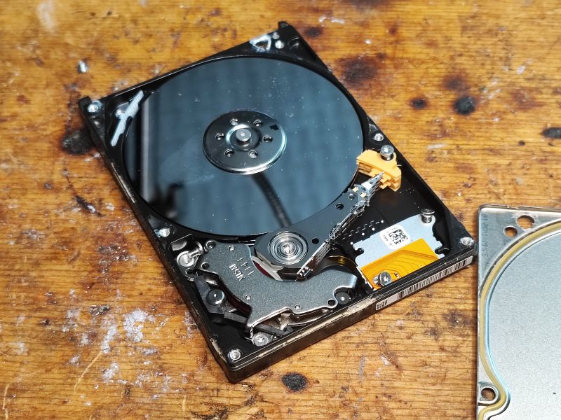Inside View of a Hard Disk Drive on a Wooden Surface Image of a hard disk drive (HDD) interior with visible platter and read/write arm on wooden surface.