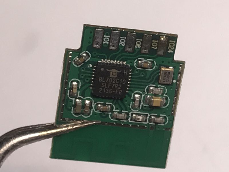 Small green circuit board held by a metal tool on a white background.