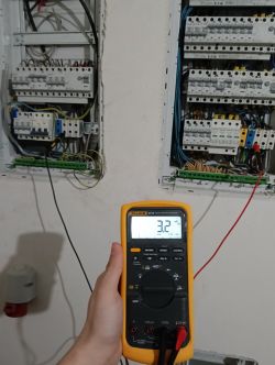 Multimetr trzymany przed otwartą szafą elektryczną z odczytem 3,2 mV.