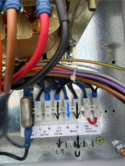 Zbliżenie na listwę zaciskową w skrzynce elektrycznej z opisanymi i oznaczonymi zaciskami oraz narysowanymi ręcznie strzałkami wskazującymi połączenia.