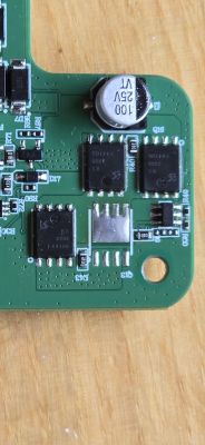 Zbliżenie na płytkę drukowaną z kilkoma komponentami elektronicznymi, w tym kondensatorem i układami scalonymi.