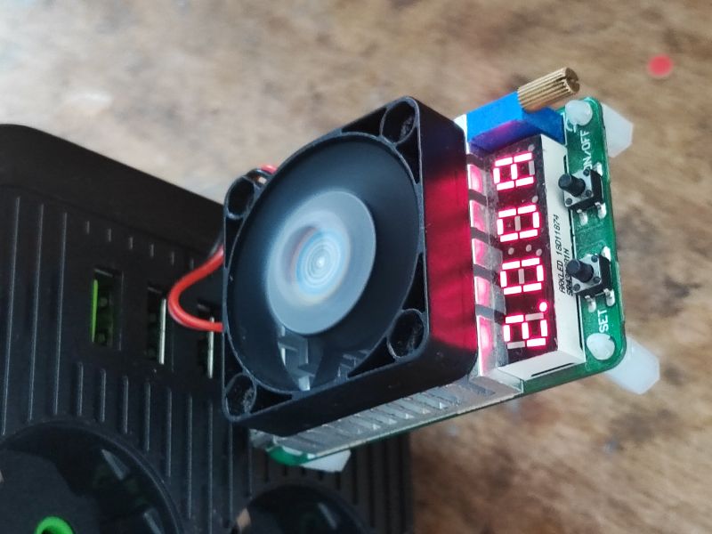 Tester USB z wyświetlaczem LED i wentylatorem podłączony do listwy zasilającej z portami USB.